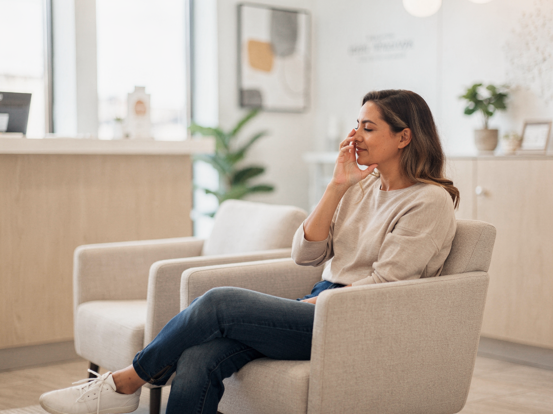 Woman sitting in a waiting room chair, touching her nose and face